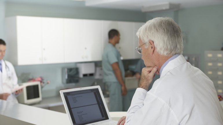 Das Bild zeigt einen Arzt, der an seinem Laptop sitzt. 