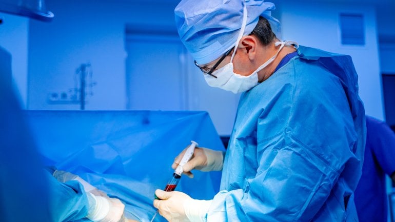 Knochenmarkspende: Chirurg entnimmt im OP-Saal Knochenmark.
