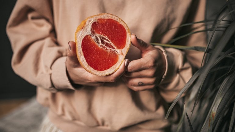 Frau hält aufgeschnittene Grapefruit in der Hand