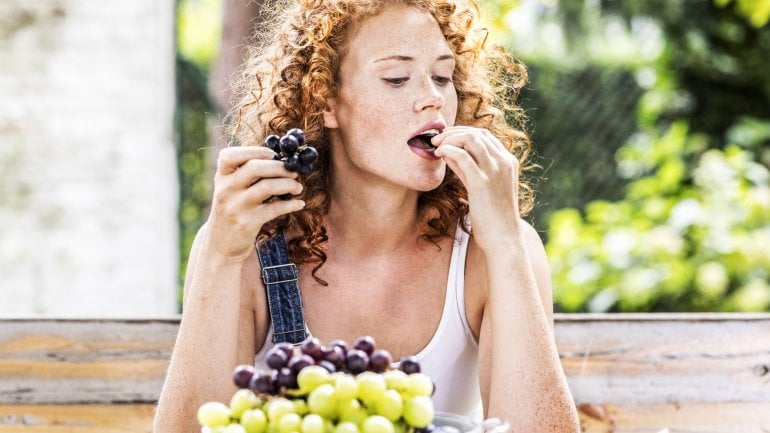 Eine junge Frau hat eine Schüssel Trauben vor sich und isst daraus