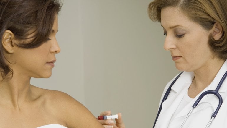 Das Bild zeigt eine Frau, die von einer Ärztin eine Spritze bekommt.