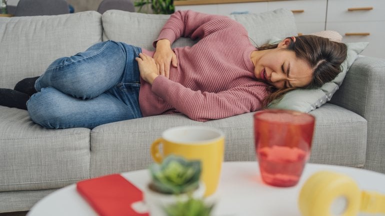 Frau mit Endometriose liegt mit Schmerzen auf dem Sofa.