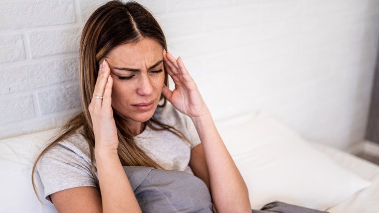 Eine junge Frau liegt mit starken Kopfschmerzen im Bett