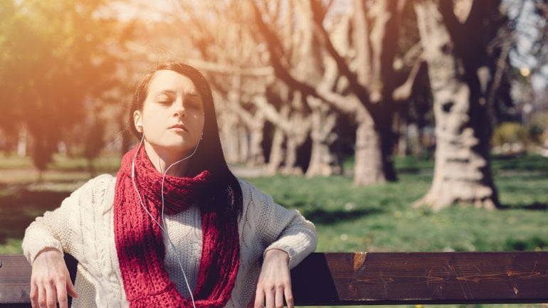 Frühjahrsmüdigkeit: Junge Frau sitzt mit geschlossenen Augen auf einer Bank und sonnt sich