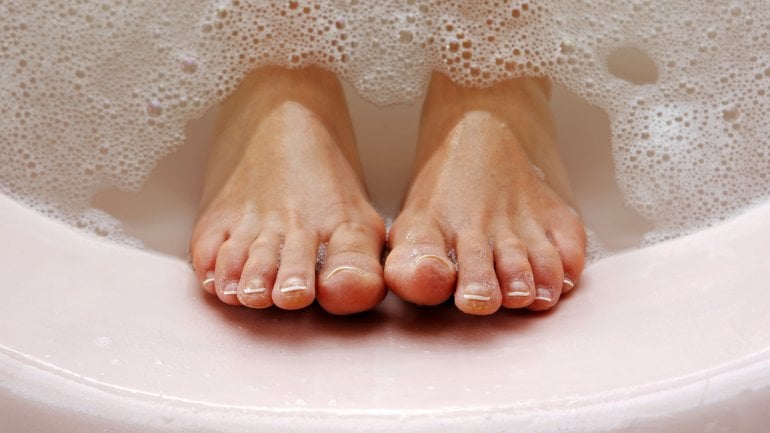 Füße in einer rosa Badewanne mit Schaum im Wasser.