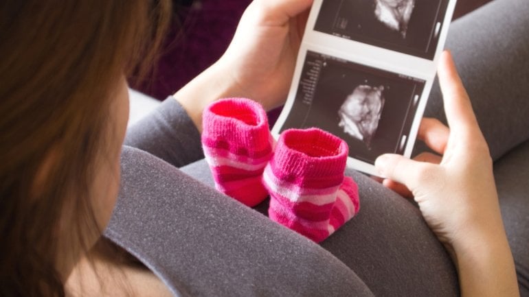 Eine schwangere Frau betrachtet Ultraschallbilder vom Baby.