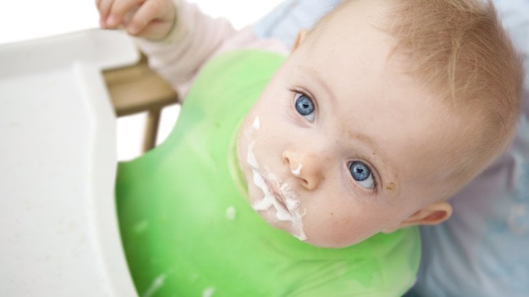 Das Bild zeigt ein Baby mit Brei im Gesicht. 