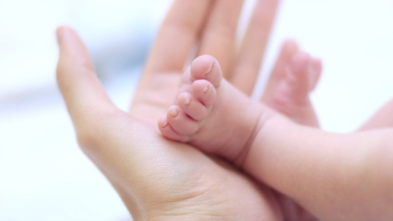 Das Bild zeigt den Fuß eines Neugeborenen in der Hand eines Erwachsenen.