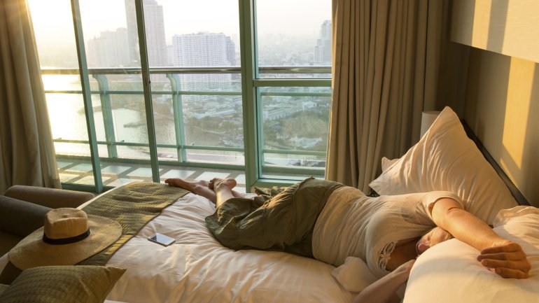 Eine Frau liegt bekleidet auf einem Bett im Hotelzimmer.
