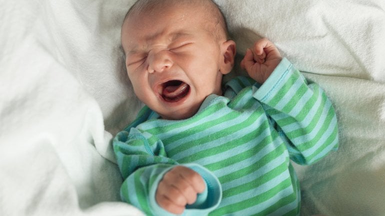 Ein Neugeborenes in grün getreiftem Oberteil weint.