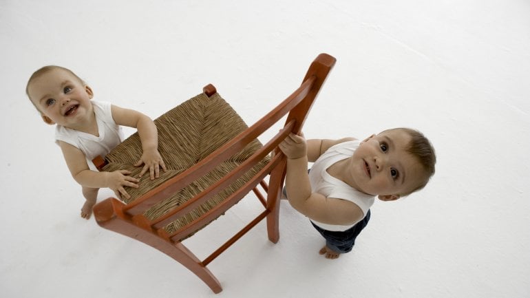 Zwei Babys stehen an einem Stuhl.