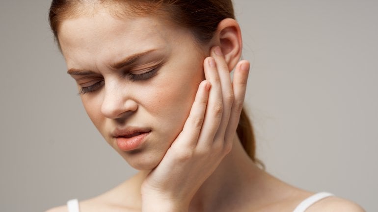 Junge Frau fasst sich ans Ohr, weil unter Ohrenschmerzen leidet.