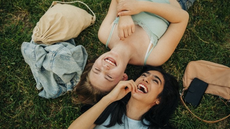 Sinnbild Pubertät: Zwei Mädchen liegen im Gras und lachen.