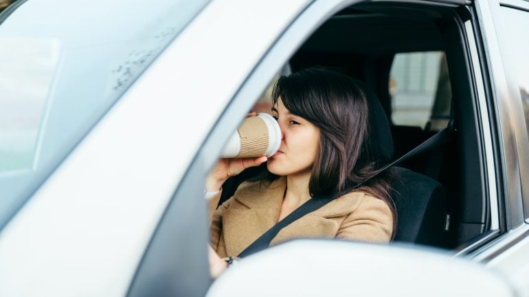 Eine Frau am Steuer eines Autos trinkt Kaffee aus einem Becher.