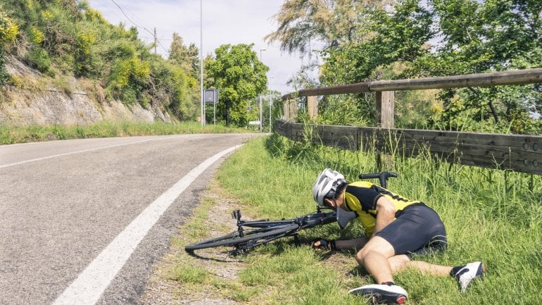 Ein Fahrradsportler ist gestürzt und liegt neben seinem Rad am Straßenrand.