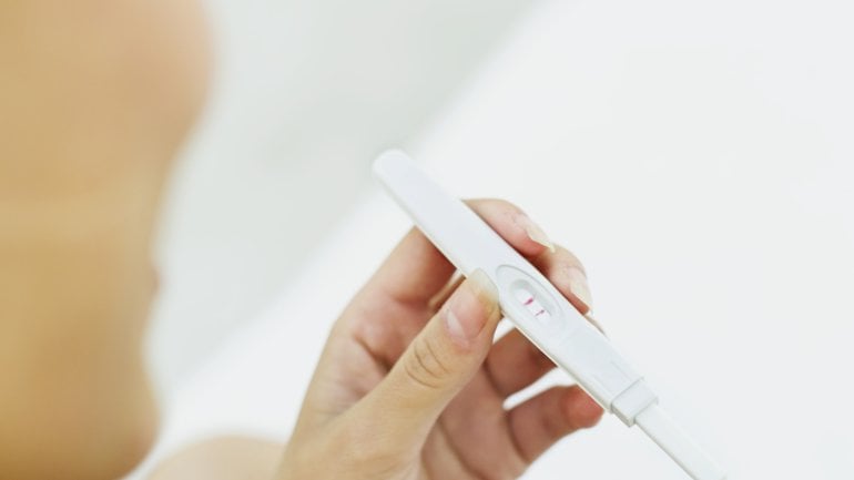 Das Bild zeigt eine Frau, die auf einen Schwangerschaftstest schaut.