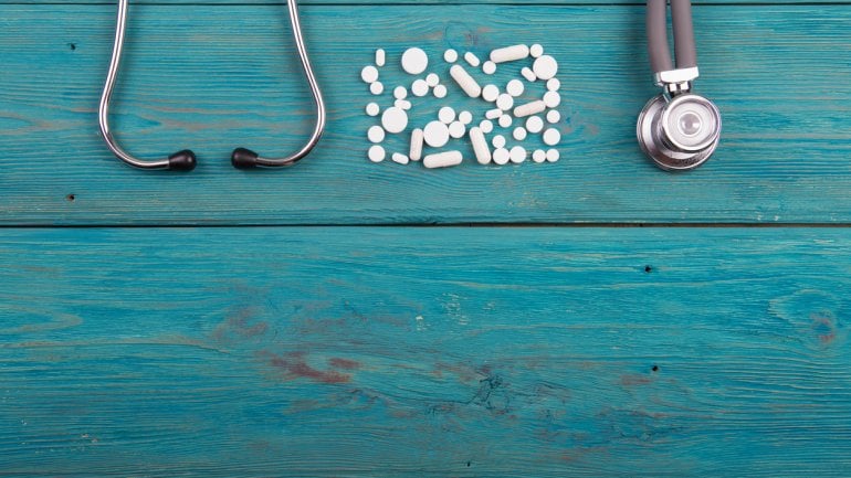 Tabletten und ein Stethoskop auf blauem Holzhintergrund.