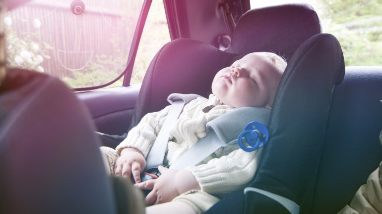 Ein Baby schläft in der Autoschale in der Sonne.