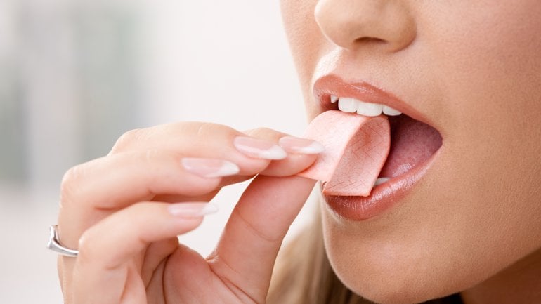 Das Bild zeigt eine Frau, die sich einen Kaugummi in den Mund steckt. 