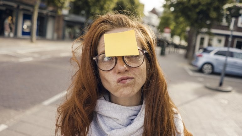 Gedächtnistraining: Eine vergesslich wirkende Frau schaut nachdenklich, ihr klebt ein Zettel auf der Stirn.