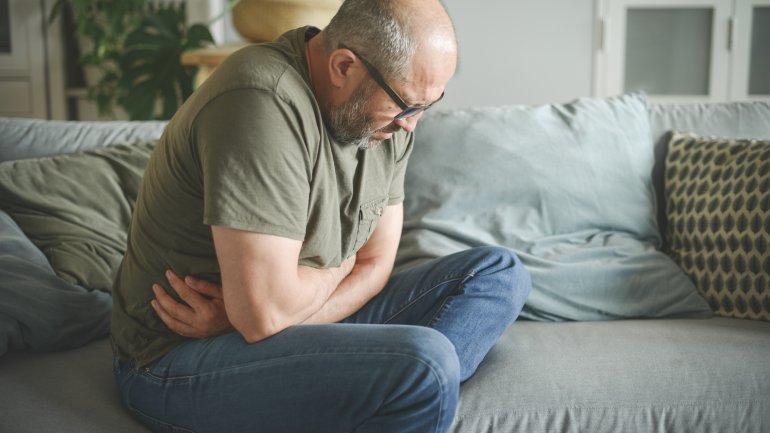 Mann mit Bauchkrämpfen auf dem Sofa möchte als Behandlung Uzarawurzel verwenden.