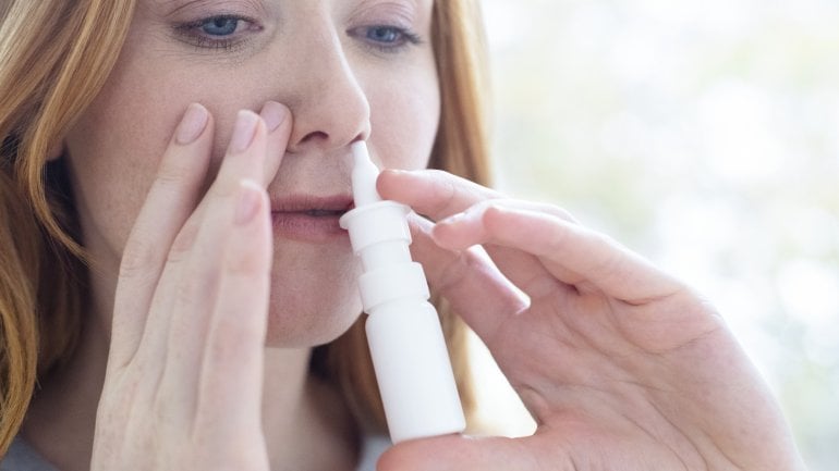 Eine Frau benutzt ein Nasenspray, weil sie gerade unter Schnupfen leidet.