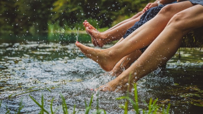 Menschen sitzen auf einem Steg und lassen ihre Beine ins Wasser baumeln. 