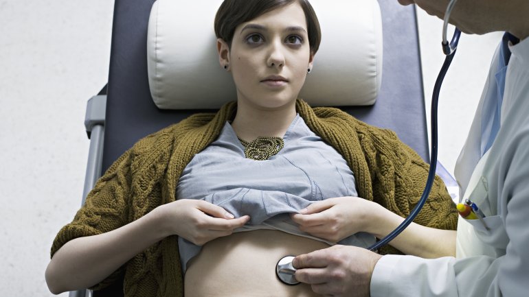 Ein Arzt untersucht eine Frau mit dem Stethoskop am Bauch.