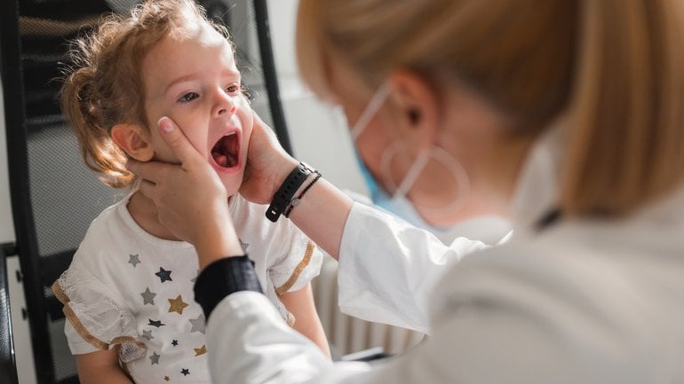 Kleines Kind mit Herpangina wird von Ärztin untersucht.