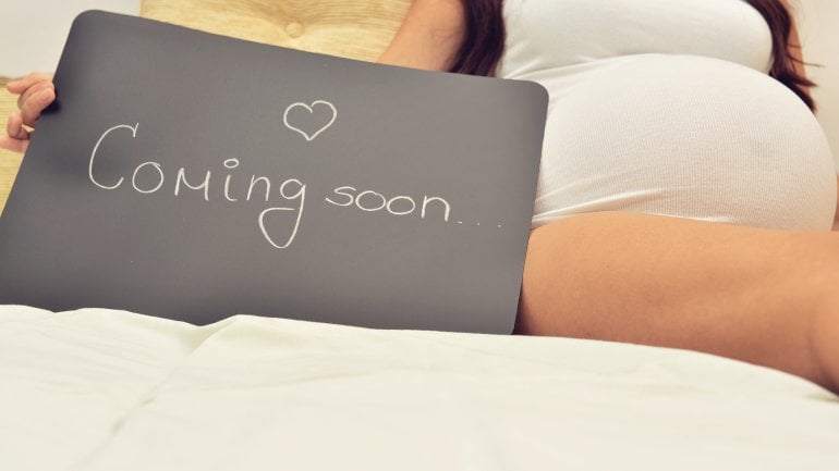 Eine Schwangere mit Schild "coming soon".