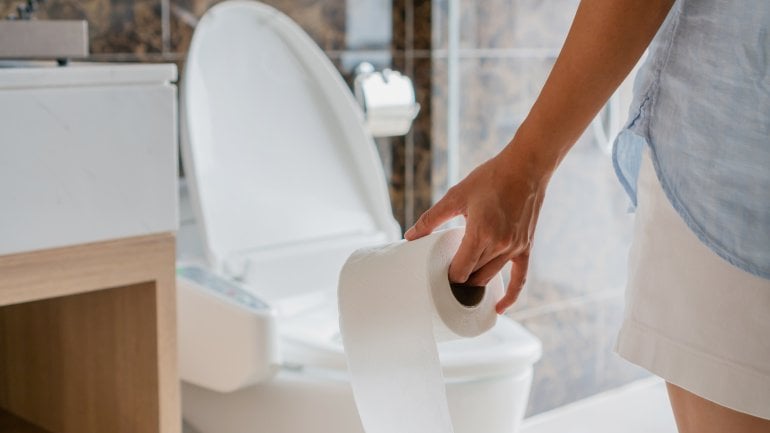 Symbolbild weißer Stuhlgang: Frau steht im Bad und hält Toilettenpapier in der Hand.