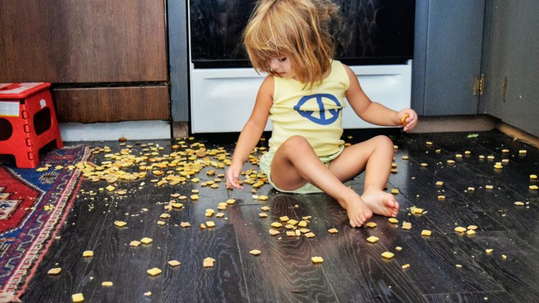 Ein Mädchen isst Knabbereien vom Boden.