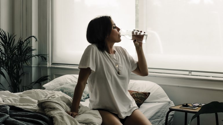 Eine Wasser sitzt auf dem Bett und trinkt Wasser aus einer kleinen Karaffe