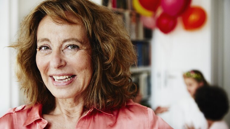 Frau mittleren Alters ist auf einer Party und schaut lächelnd in die Kamera, im Hintergrund sind Luftballons zu sehen