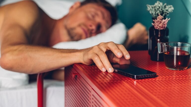 Pornosucht: Mann greift im Bett nach Handy