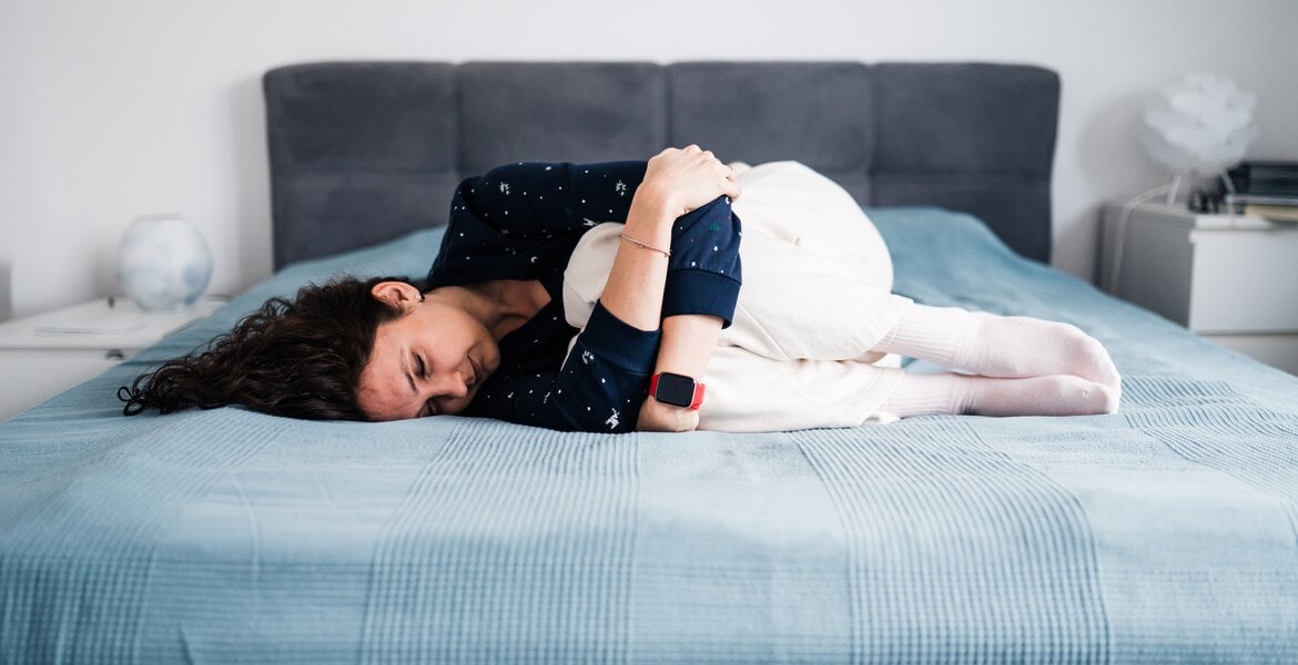 Frau mit chronischen Schmerzen liegt gekrümmt auf dem Bett