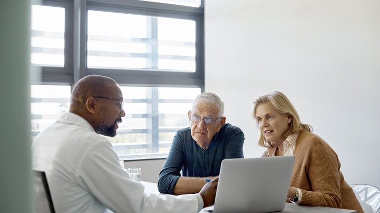 Paar mittleren Alters sitzt im Sprechzimmer und spricht mit einem Arzt über die Teilnahme an einer klinischen Studie