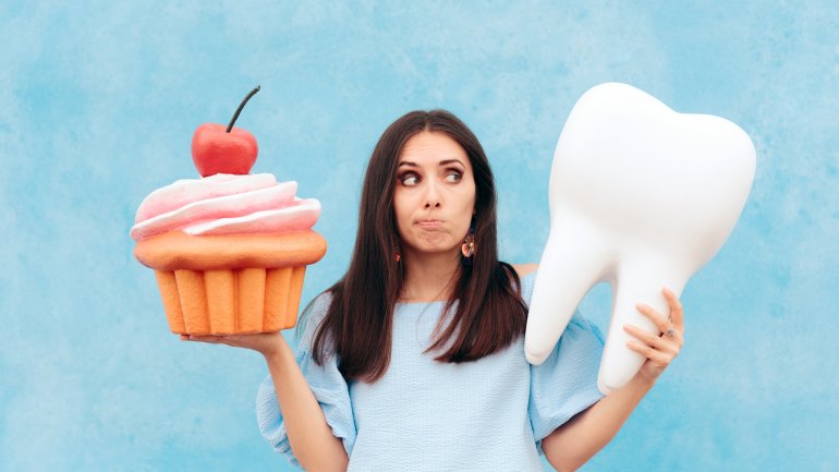 Eine Frau hält einen künstlichen Cupcake in der einen Hand und einen riesigen Zahn in der anderen Hand.