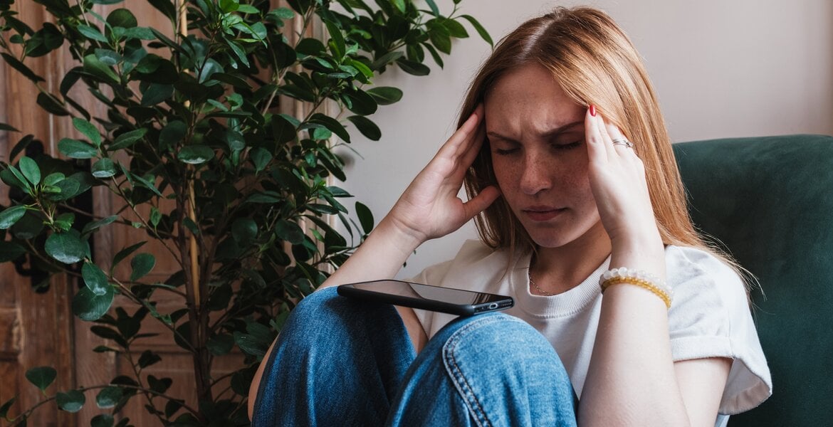 Eine junge Frau sitzt gestresst auf dem Boden und greift sich mit beiden Händen an die Schläfen.