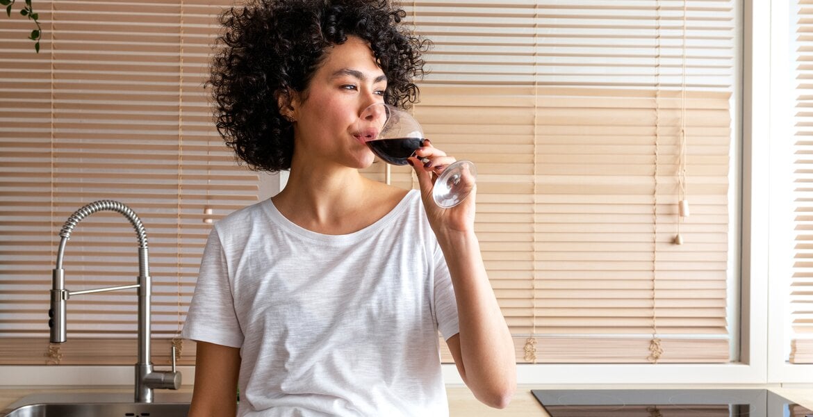 Eine nachdenkliche junge Frau trinkt in der Küche Wein.