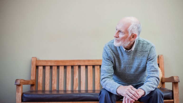 Ein älterer Mann sitzt auf einer Holzbank.