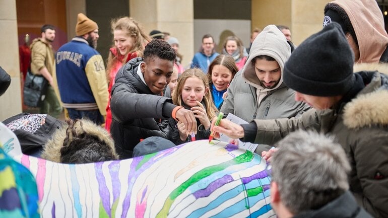 In der Münchner Innenstadt bemalen Menschen die Streifen eines Zebras bunt.