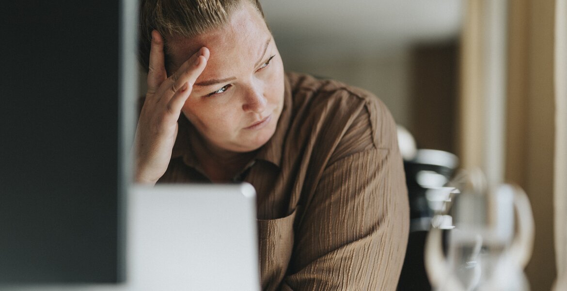 Eine junge Frau sitzt am Schreibtisch und schaut mit leerem Blick in die Ferne.