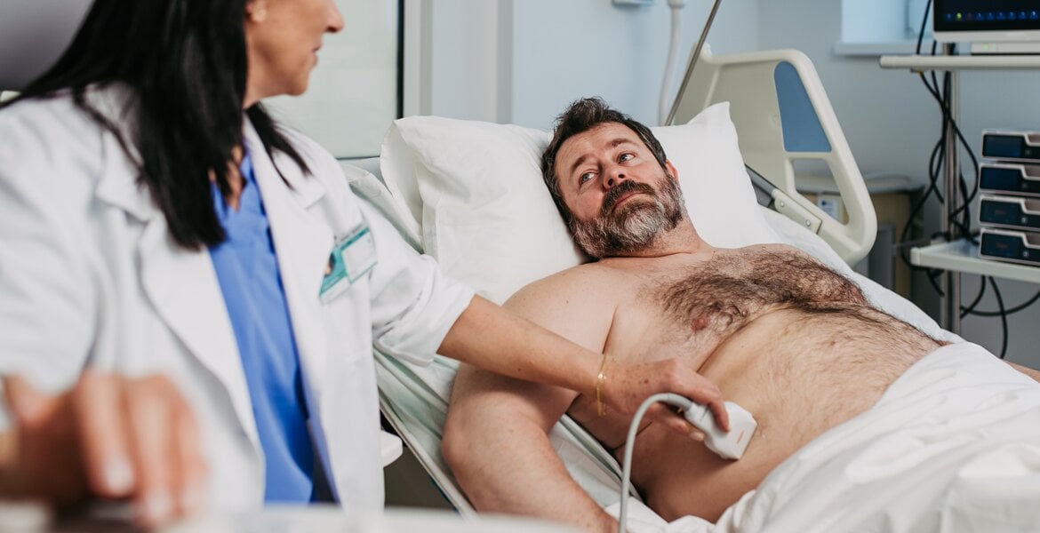 Ein Mann wird von einer Ärztin an der Leber mit Ultraschall untersucht.