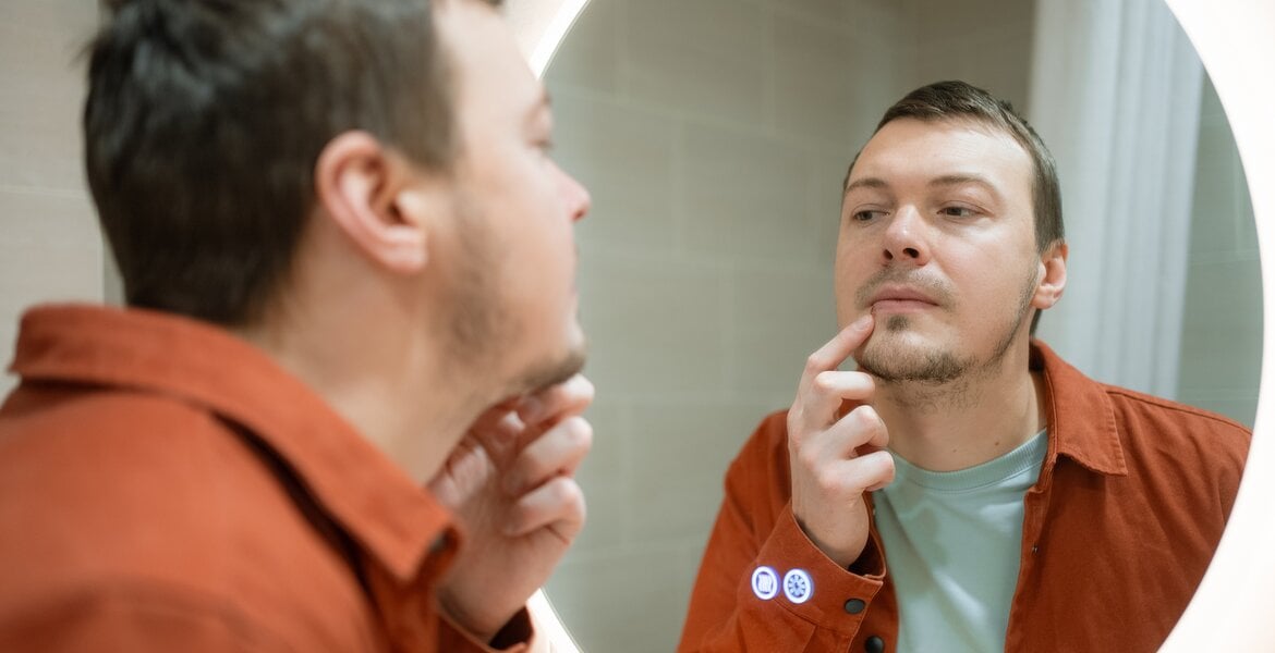 Ein junger Mann schaut im Spiegel seine Lippen an.