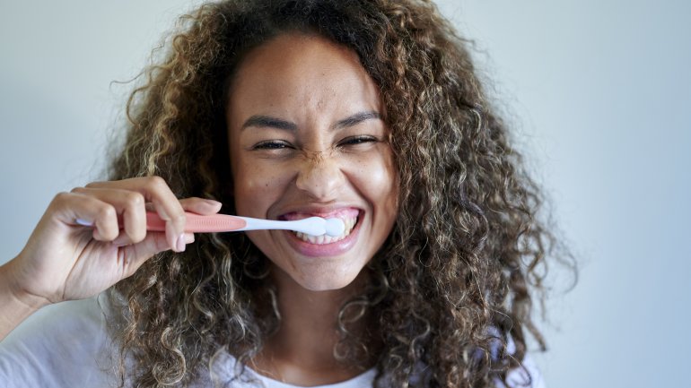 Eine Frau putzt sich lachend die Zähne.