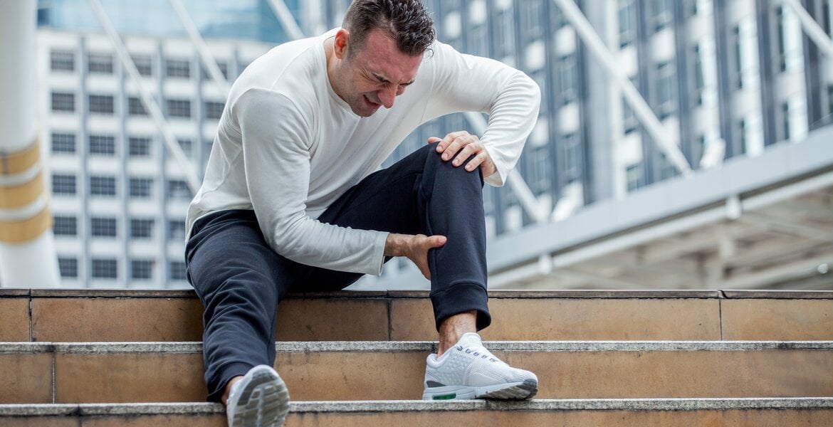 Ein Mann sitzt mit Muskelschmerzen auf einer Treppe.