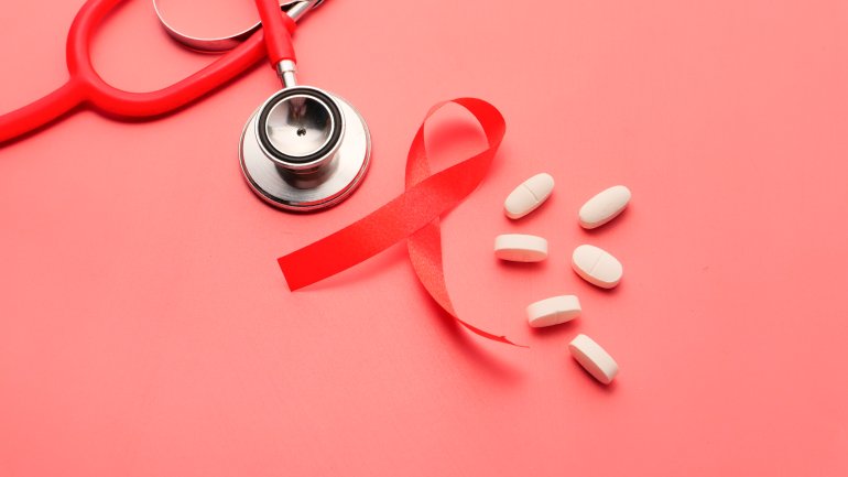 Man sieht eine Aidsschleife auf rotem Hintergrund neben Tabletten und einem stethoskop 