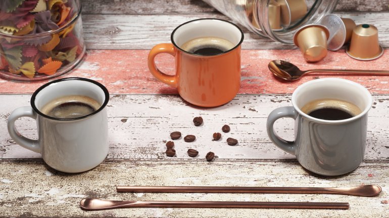 Das Bild zeigt drei Kaffeetassen, Kaffeebohnen und Kaffeekapseln.