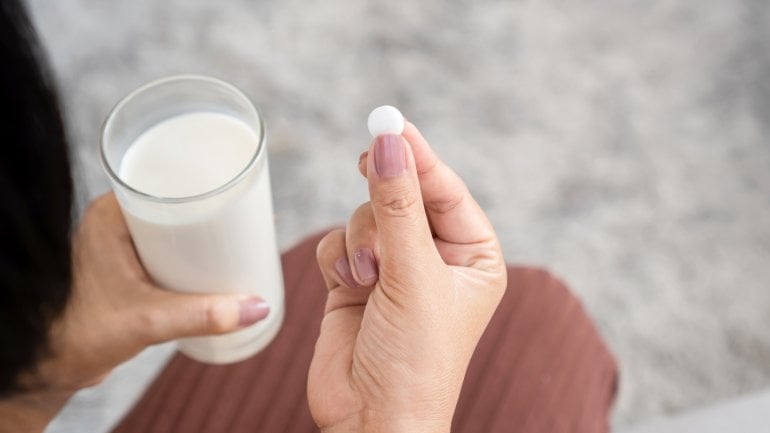 Man sieht zwei Hände: In der einen ein Glas Milch, in der zweiten Antibiotika-Tabletten
